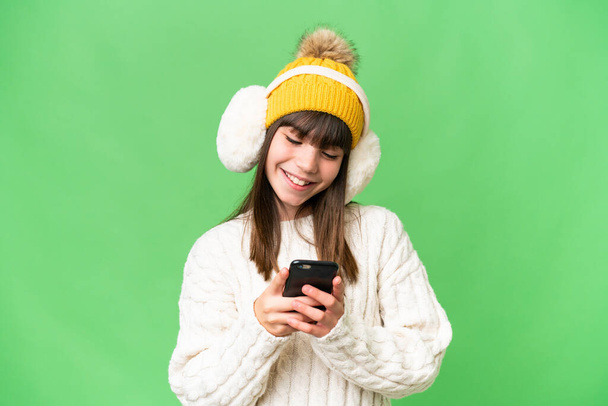 İzole edilmiş arka planda kışlık kuklalar takan küçük beyaz kız cep telefonuyla bir mesaj gönderiyor. - Fotoğraf, Görsel