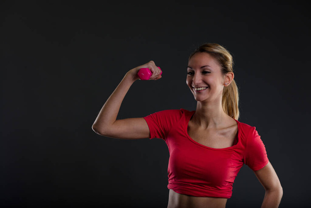 Stolze, glückliche Blondine, die eine rosafarbene Hantel hebt, tägliches Training. Flacher Bauch, durchtrainierter Körper. Anstrengung und Engagement führen zu Ergebnissen - Foto, Bild
