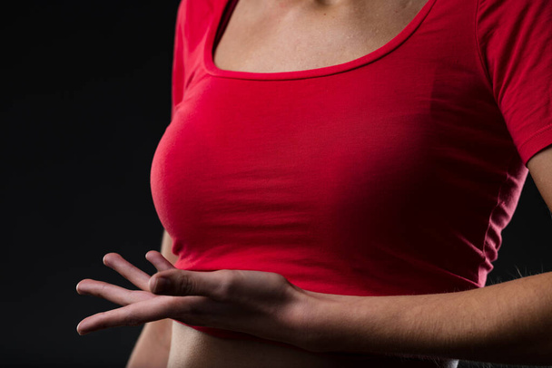 Woman's breast, hand underneath stressing importance of care, prevention, pap test, breastfeeding, cosmetic issues, surgery, mastectomy. Intense red shirt, caring hand gesture - dark background - Foto, afbeelding