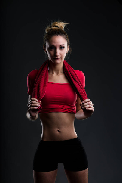 Portrait of an attractive girl in gym attire, proud of her flat stomach. She wears a red top and black leggings. 'If I like attractive and fit people, why should it be any different for others towards - Valokuva, kuva
