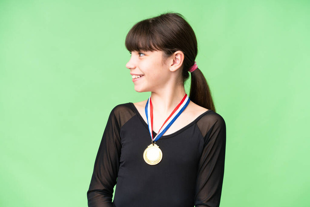 Pequeña chica caucásica con medallas sobre fondo aislado mirando lado - Foto, Imagen