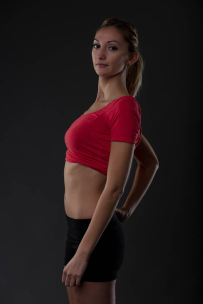 Fit woman, toned body. Gym workouts reflect determination, responsibility. Portrait of blonde girl in red shirt, flat belly, black shorts - Foto, afbeelding