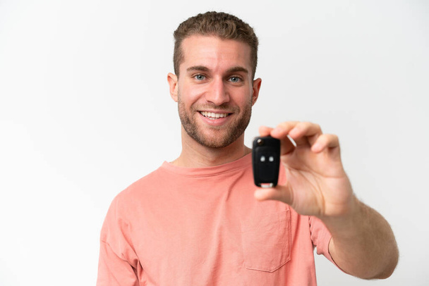 Νεαρός καυκάσιος άνδρας που κρατά τα κλειδιά του αυτοκινήτου απομονωμένα σε λευκό φόντο με χαρούμενη έκφραση - Φωτογραφία, εικόνα