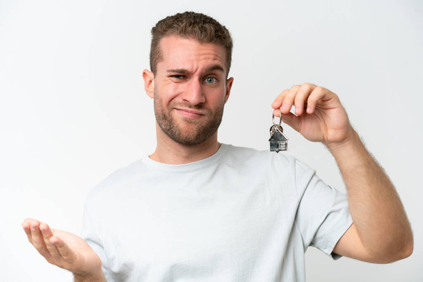 Young caucasian man holding home keys isolated on white background saluting with hand with happy expression - Foto, imagen
