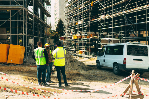  ISTANBUL, TÜRKEI - 22. Mai 2022: Vor dem Hintergrund des im Bau befindlichen Gebäudes stehen zwei junge Arbeiter in Overalls mit dem Rücken zum Neubau.Baukonzept.  - Foto, Bild
