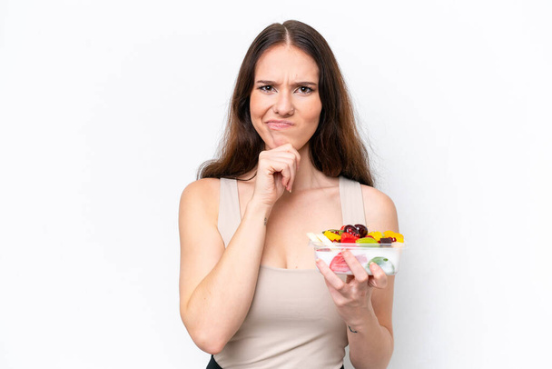 Молода біла жінка тримає миску з фруктами ізольовано на білому тлі має сумніви та мислення
 - Фото, зображення