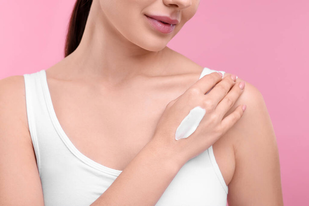 Woman with smear of body cream on her hand against pink background, closeup - Zdjęcie, obraz