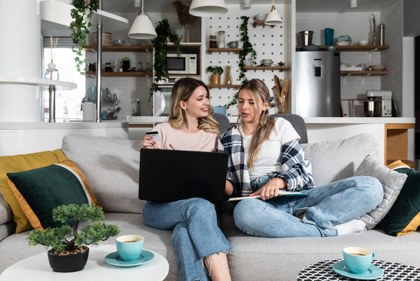Two young women and best friends doing some online shopping at home with a laptop and a credit card from online web shop sale while they smiling and they are happy - Photo, image