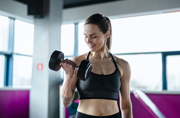 Mujer joven haciendo ejercicio con pesas en un club de salud - Foto, Imagen