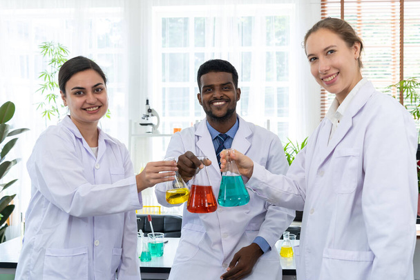 The scientist team talking about liquid research experiment in laboratory, Young scientist and female colleagues holding difference color liquid in beaker in hand together at science lab, copy space - Foto, Imagem