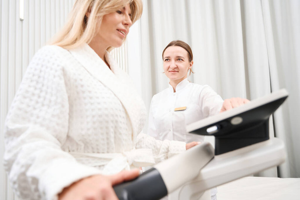 Woman in a medical center undergoes a bioimpedancemetry diagnostic procedure, a medic uses modern equipment - Foto, Imagen