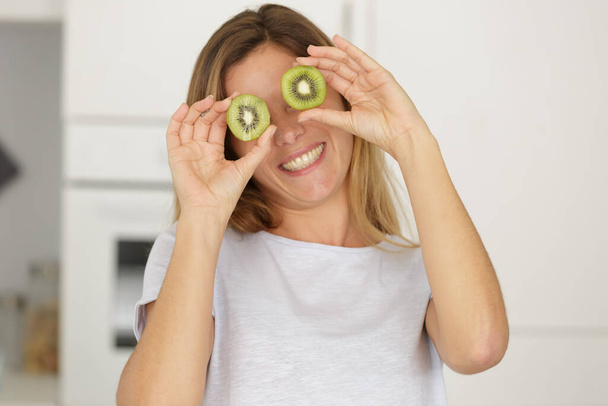 woman with kiwi slices in front of her eyes - Фото, изображение