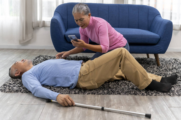 Asian senior man lay unconscious on the floor in living room. His wife used smartphone to call an ambulance to help him. copy space - Foto, imagen