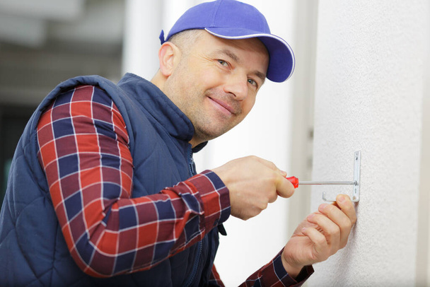 builder using screwdriver screws a wall - Foto, Imagen
