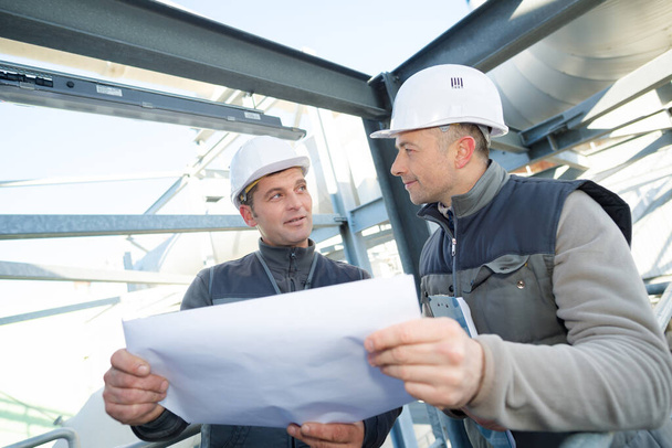 supervisor with workers examining blueprints at table in industry - Zdjęcie, obraz