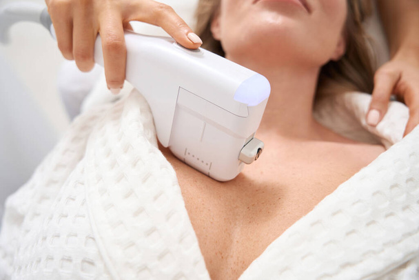 Woman on the procedure of non-surgical skin tightening in the decollete area, the cosmetologist uses a modern apparatus - Photo, Image