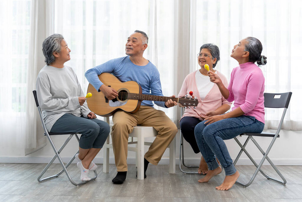 Happy moment with Group of Asian senior man playing guitar and woman singing and dance with fun togetherness in living room at nursing home - Foto, Imagem