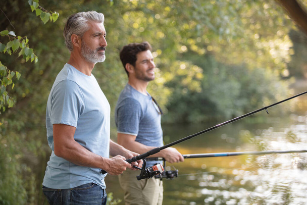 father and adult son fishing lakeside - Фото, зображення