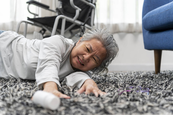 Asian crippled senior woman has accident fell from wheelchair lay on the carpet in house, Trying to reach for a pill bottle, accident of seniors when they are alone, copy space. - Foto, afbeelding