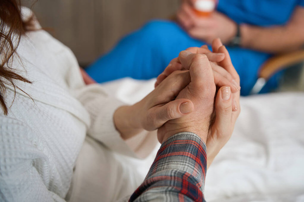 Close up view of two people on sick bed holding hand of each other indoors - Foto, Imagem