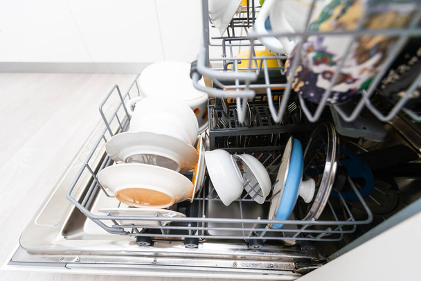 Nyitott mosogatógép tiszta edényekkel a fehér konyhában. - Fotó, kép