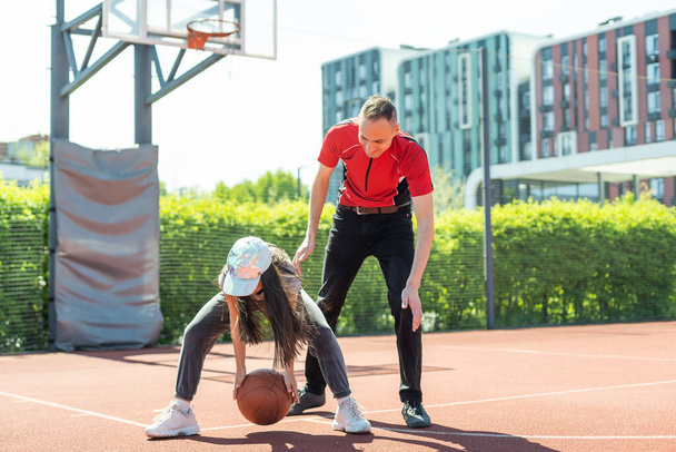 Happy father and teenage daughter playing basketball outside at court. - Foto, afbeelding