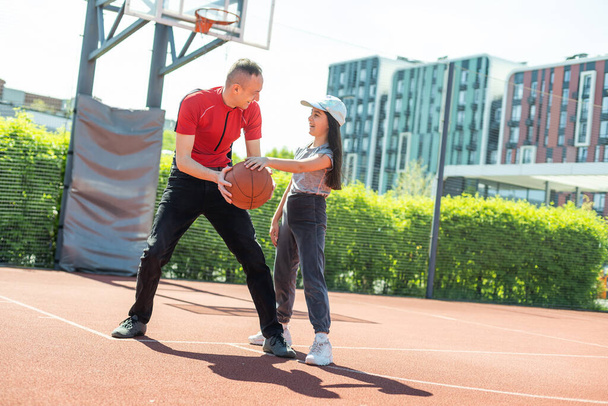 Happy father and teen daughter embracing and looking at camera outside at basketball court - 写真・画像