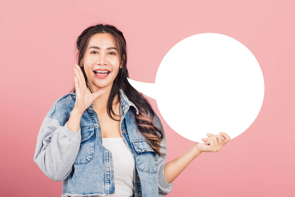 Happy Asian beautiful young woman smiling excited wear denims hand near mouth announce news and holding empty speech bubble sign, Portrait female posing idea, studio shot isolated on pink background - Φωτογραφία, εικόνα
