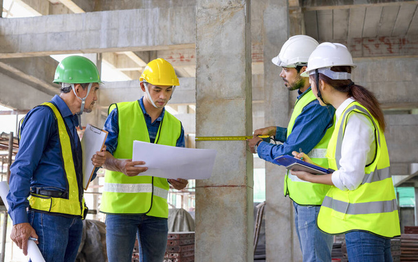 projektový manažer inženýr měřící pilíř s páskovým měřením, tým inženýrů pracující v budově ve výstavbě, kontrolující konstrukční standardy výstavby nové budovy. - Fotografie, Obrázek