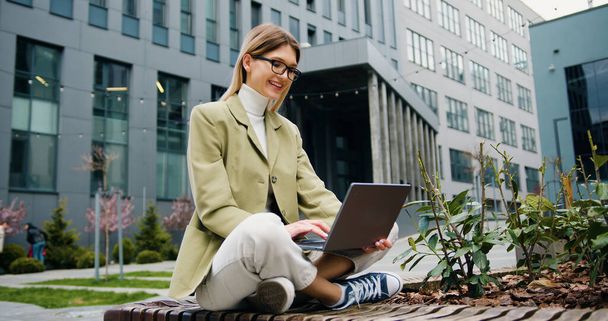 Successful young caucasian female freelancer typing on keyboard using laptop computer. Outdoors. Online working - 写真・画像
