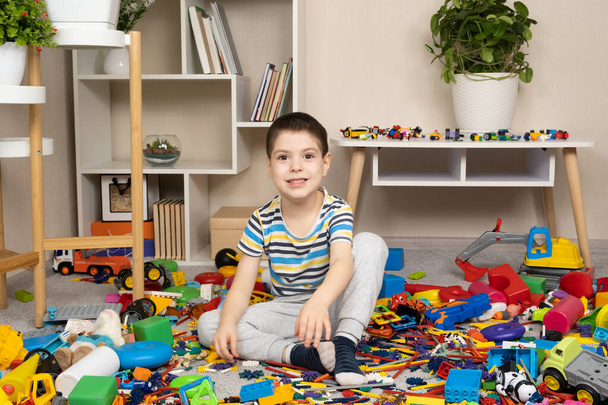Little boy playing with toys sitting on the floor among scattered toys, a mess in the childrens room. - Photo, Image