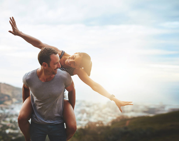 Travel, happy couple with piggyback ride and mountain outdoors with lens flare. Sunshine or mockup space, nature adventure or freedom and people playing on holiday break or summer vacation together - Фото, изображение