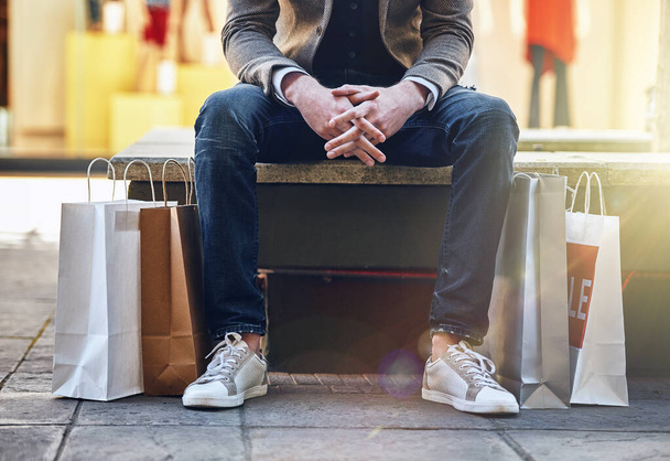 City, man sitting and sale with shopping bags on floor, sidewalk or street with sneakers, relax or waiting for taxi. Guy, retail and fashion on bench in metro cbd with discount, promotion or clothes. - Φωτογραφία, εικόνα