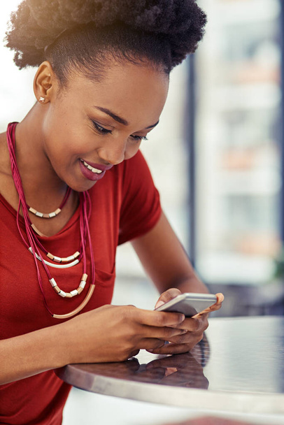Telefon, mosoly és fekete nő sms az asztalnál, online böngészés vagy internet étteremben. Mobiltelefon, boldog és afrikai női személyek hálózatba szervezése, közösségi média és web görgetés a mobiltechnológiáról - Fotó, kép