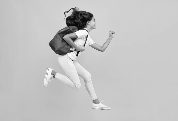 Amazed teen girl. School girl in school uniform with school bag. Schoolchild teenager hold backpack on yellow isolated background. Run and jump. Excited expression, cheerful and glad - Φωτογραφία, εικόνα