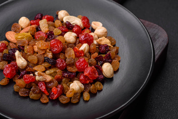 Mélange de noix de cajou rôties, noisettes et noix avec canneberges séchées et raisins secs sur un fond de béton foncé - Photo, image
