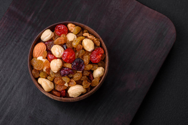 Mix of roasted cashews, hazelnuts and walnuts with dried cranberries and raisins on a dark concrete background - Foto, Imagen
