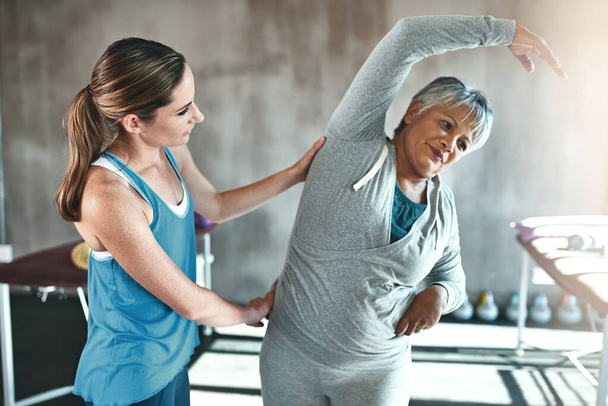 Stretching, help and old woman with personal trainer for fitness, wellness or rehabilitation. Health, workout or retirement with senior patient and female trainer in gym for warm up training. - Foto, Imagem