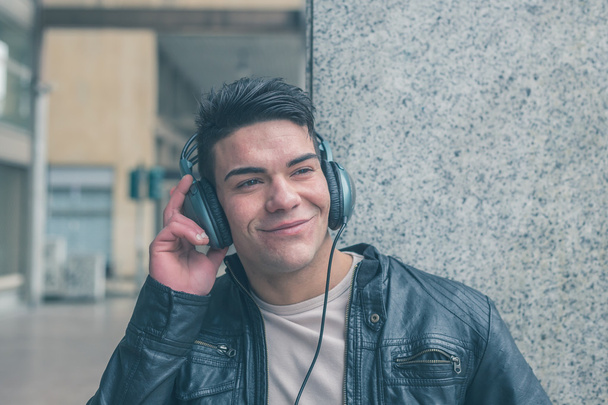 Молодий красивий чоловік з навушниками позує на міських вулицях
 - Фото, зображення