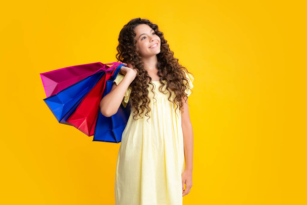 Szczęśliwy portret nastolatki. Piękna nastolatka moda dziewczynka z torby na zakupy na żółtym tle. Zakupy i moda. Dzieciak z torbami na zakupy. Uśmiechnięta dziewczyna - Zdjęcie, obraz