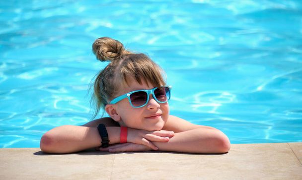 Portrait of happy child girl relaxing on swimming pool side on sunny summer day during tropical holidays. - Foto, Imagen