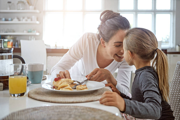 Mother, child and pancakes for breakfast in a family home with love, care and happiness at a table. A happy woman and girl kid eating food in plate together in morning for health and wellness. - Photo, Image