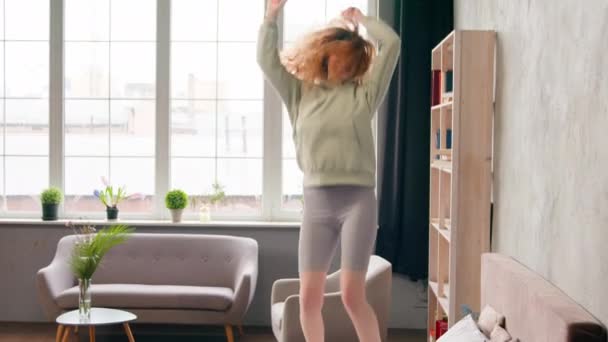 Счастливая беззаботная беззаботная белая женщина-арендодательница домовладелица развлекается дома, прыгает в спальню и празднует утренний прыжок, танцуя под музыкальный отель - Кадры, видео