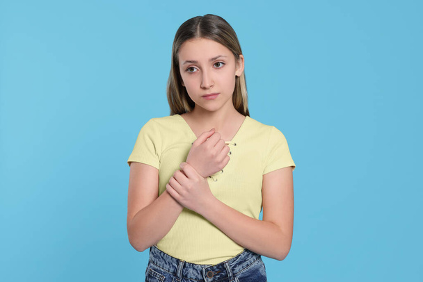 Teenage girl suffering from pain in wrist on light blue background. Arthritis symptom - Фото, изображение