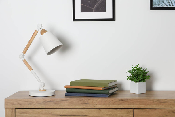 Desk lamp, books and houseplant on wooden chest of drawers indoors - Valokuva, kuva