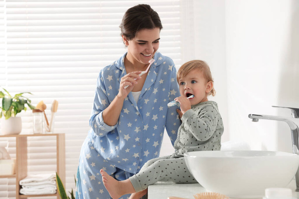 Mother and her daughter brushing teeth together in bathroom - Foto, afbeelding
