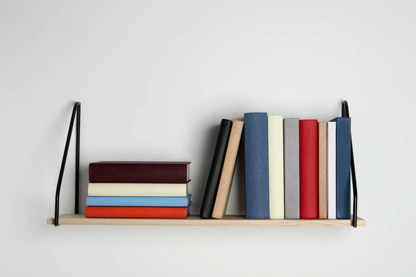 Wooden shelf with many hardcover books on white wall - Foto, immagini
