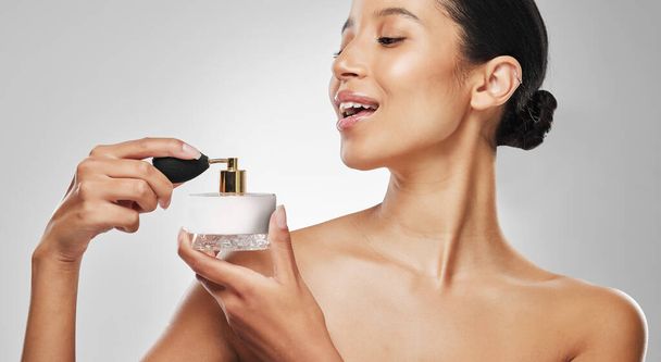 No hay elegancia posible sin perfume. Foto de estudio de una joven atractiva que aplica perfume sobre un fondo gris - Foto, imagen