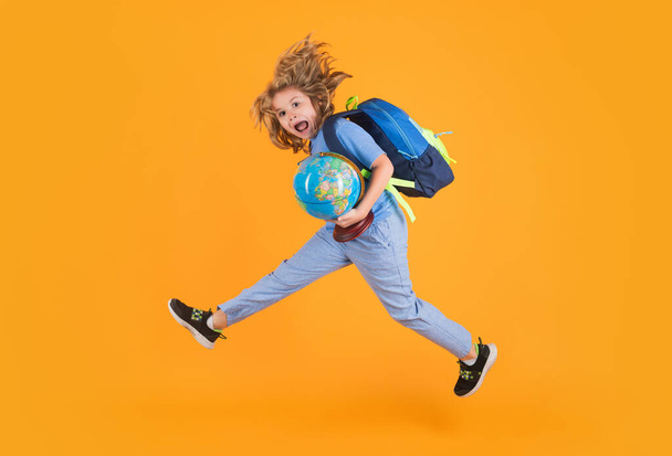 Shool kid jump with school bag and globe. School child in school uniform with bagpack and globe jump. School children jumping on studio isolated yellow background - Foto, Imagen
