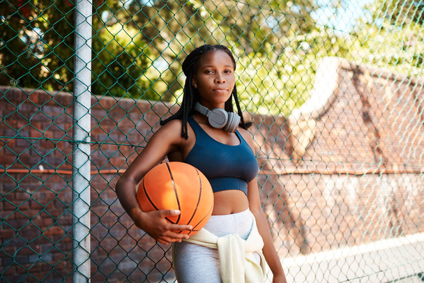 Credi nel basket. Ritratto di una giovane donna sportiva che tiene in mano un pallone da basket mentre si trova contro una recinzione all'aperto - Foto, immagini